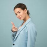 Una mujer joven con un traje azul muestra confianza con una pose relajada sobre un fondo azul.