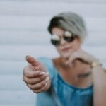 Mujer de moda con gafas de sol extiende la mano, un gesto atractivo.