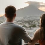 Una pareja joven comparte un momento romántico, con vistas al paisaje urbano y a las montañas de Monterrey al atardecer.