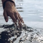 Un primer plano sereno de una mano que toca suavemente la superficie de un agua brillante a la luz del día.