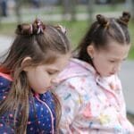 Dos chicas jóvenes con chaquetas de invierno, contemplativas en un entorno de parque.