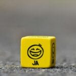 Primer plano de un dado amarillo con un emoticono de cara sonriente que simboliza la felicidad y la diversión.