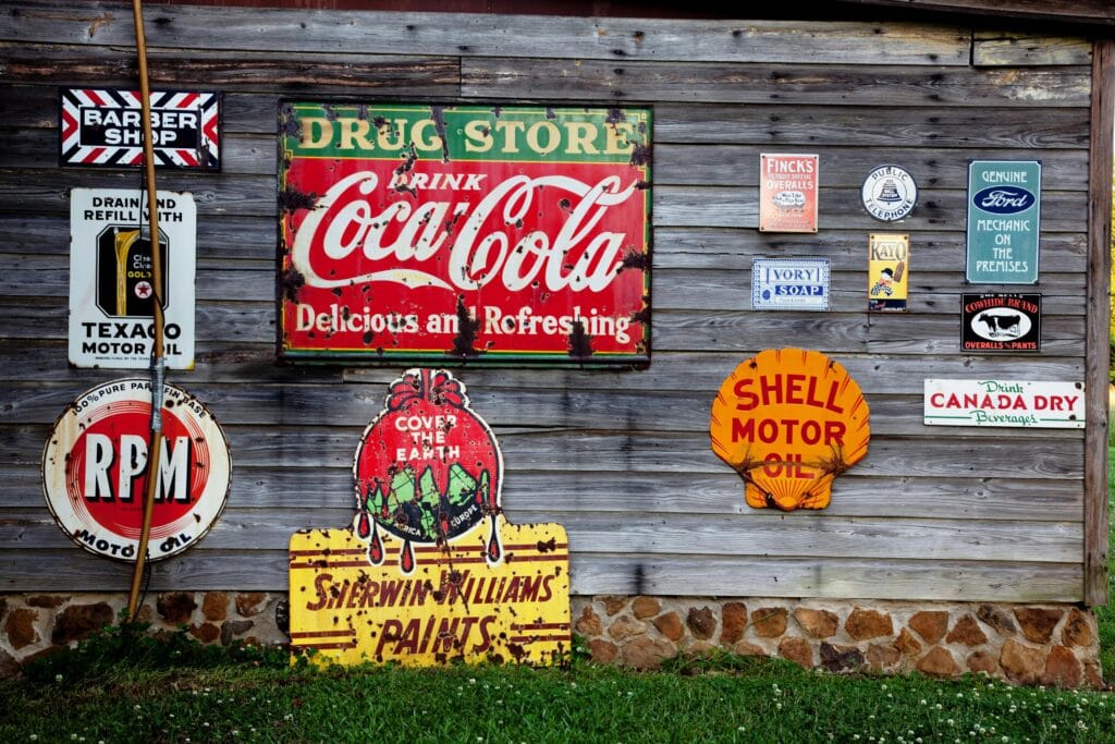 Colección de carteles publicitarios vintage en una pared rústica de madera que muestran marcas clásicas.