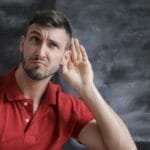 Thoughtful man listening intently against a chalkboard background in a red polo shirt.