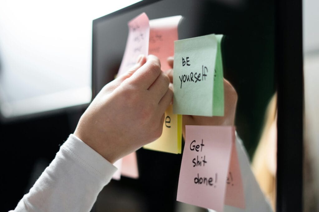 Primer plano de la mano colocando coloridas notas adhesivas motivacionales en un espejo, mensajes inspiradores.