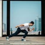 Toma dinámica de un joven corriendo al aire libre en un entorno urbano con rascacielos de fondo.