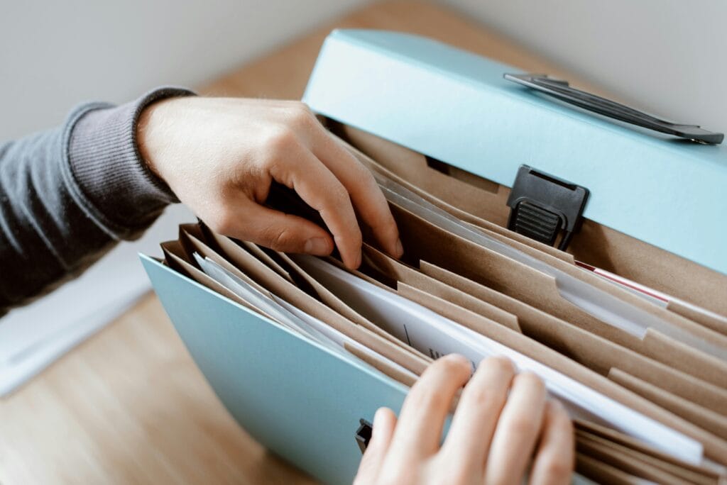 Primer plano de manos organizando papeles en una carpeta azul, ideal para conceptos de negocios y oficina.