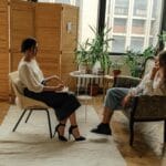 Dos mujeres se sientan en una sesión de terapia, creando un ambiente tranquilo y profesional.