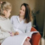 Una mujer y un niño sentados juntos, leyendo un libro Braille dentro de una habitación acogedora.