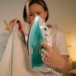 Asian woman ironing indoors experiencing an ironing fail with a burned garment. Captures frustration.