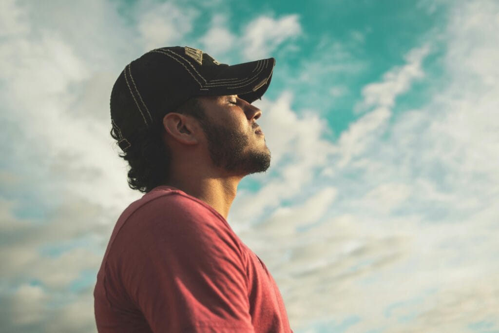 Un hombre disfruta de la relajación al aire libre y la atención plena bajo un cielo brillante y nublado, exudando calma y paz.
