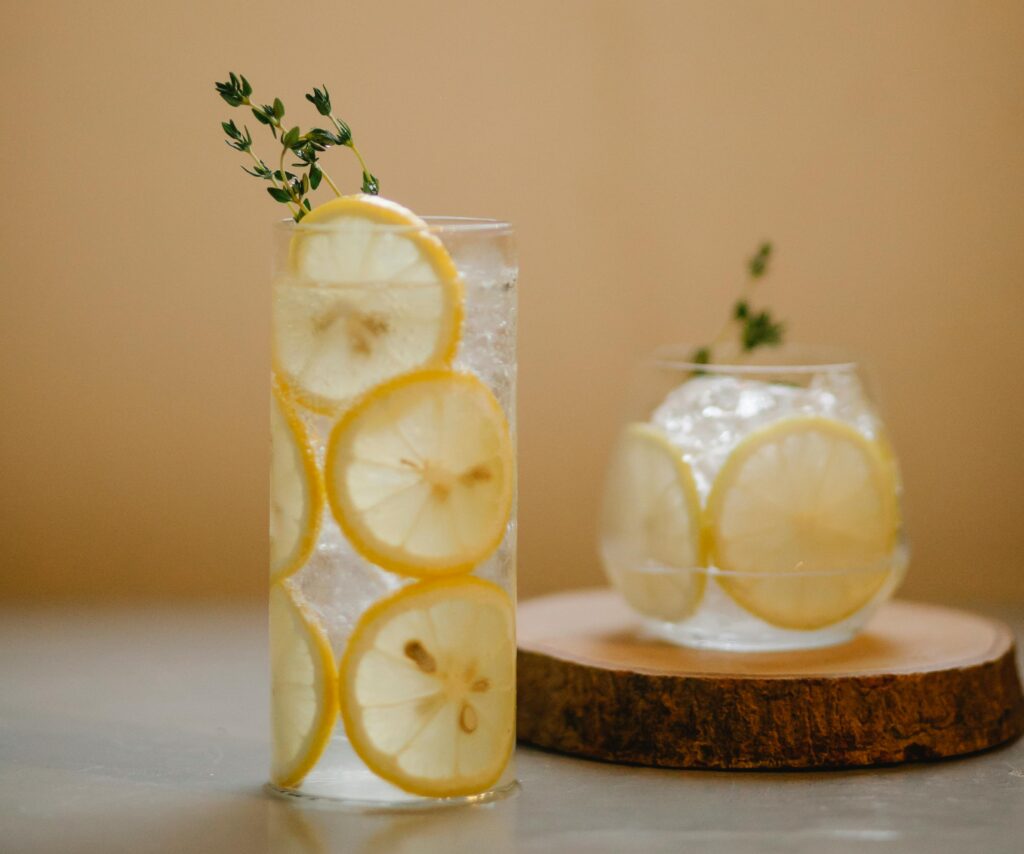 Una bebida fresca y refrescante con rodajas de limón y tomillo en vasos transparentes en un posavasos de madera.