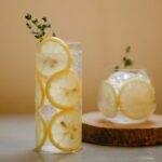 Una bebida fresca y refrescante con rodajas de limón y tomillo en vasos transparentes en un posavasos de madera.