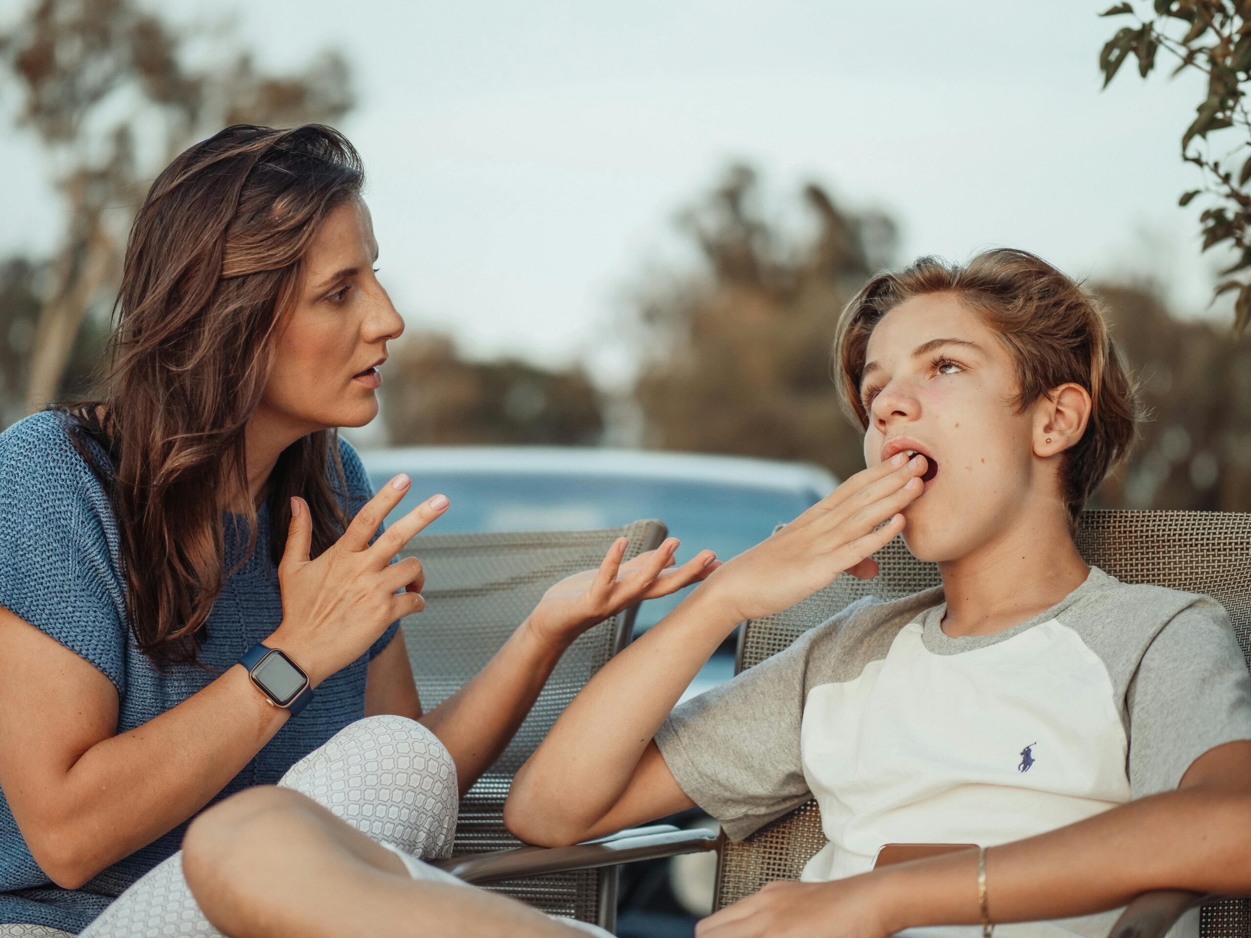 Una madre y su hijo adolescente están teniendo una conversación al aire libre. El hijo parece desinteresado.