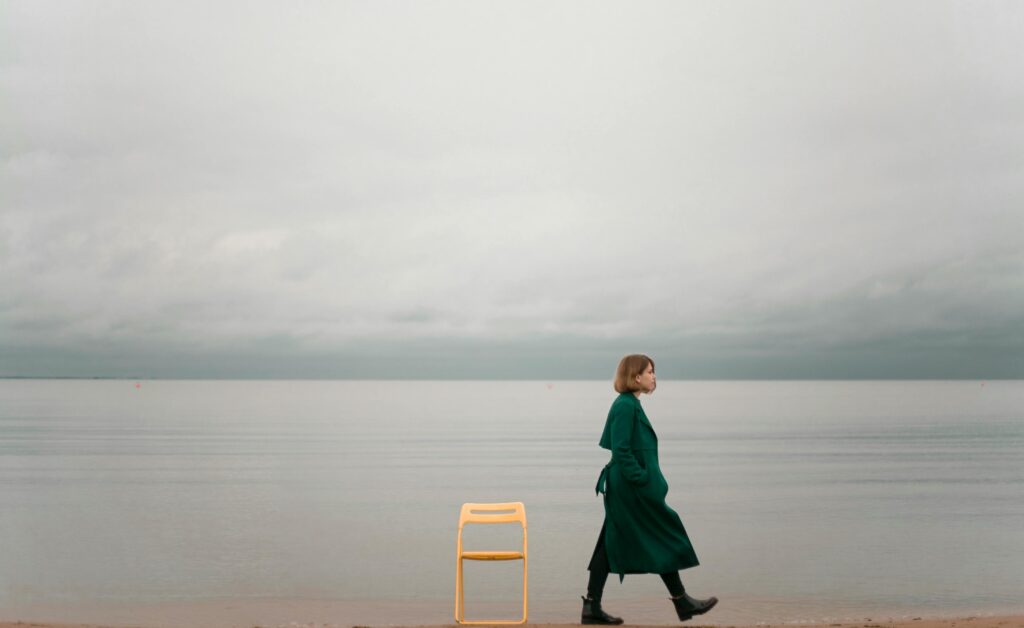 A solitary woman walks by the ocean, capturing calm and introspective solitude.